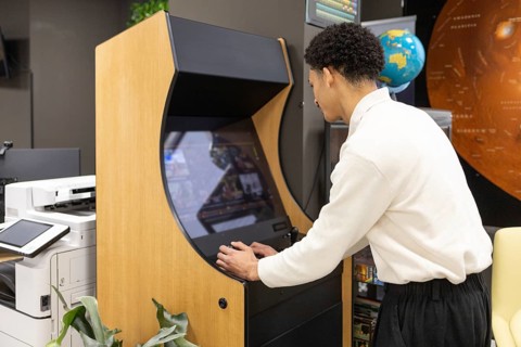 An employee plays on a retro arcade gaming machine during a break in a modern office. Surrounding