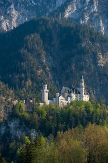 Historic Neuschwanstein Castle is enthroned on a hill, surrounded by mystical, wooded mountains in