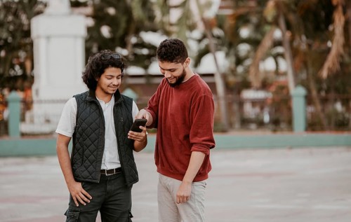 Two happy friends using the mobile phone on the street. Portrait of two smiling guys using cell