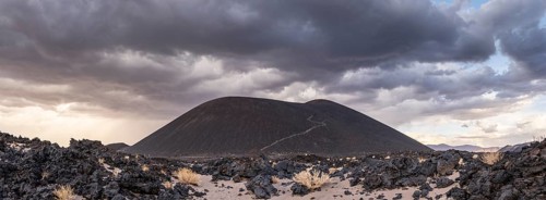 A volcanic hill rises under dramatic clouds in the middle of a rocky desert, Argentina, volcanoes,