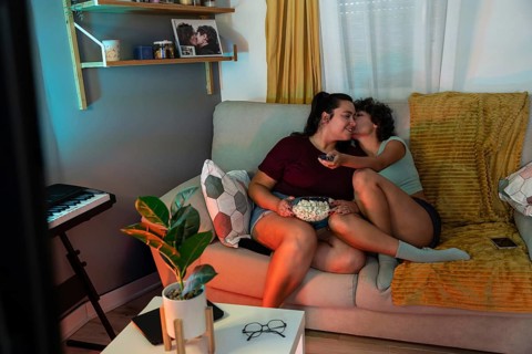 A loving lesbian couple relaxes on a couch, sharing popcorn during a cozy movie night. The