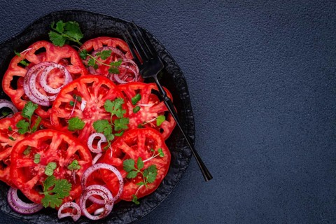 Freshly sliced tomatoes and red onions, garnished with herbs, on a black plate, summer salad, no