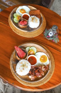 Two plates featuring filipino breakfast with fried eggs, rice, meat, watermelon, tomato, cucumber,