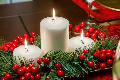 Three tiered candles with garland and holly berries decorate Christmas holiday table