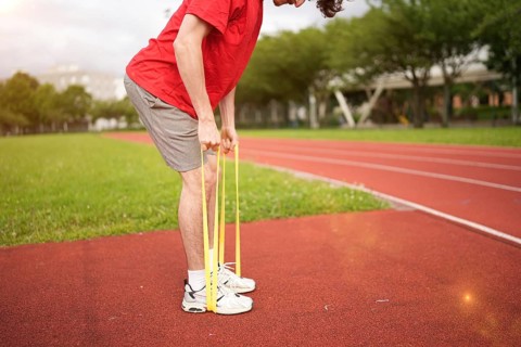 Lower section of an unrecognizable caucasian sportive young man warming up with elastic band in a