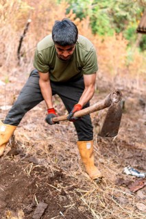 A man engaging in farm work, digging soil with a hoe in the rural Colombian countryside,