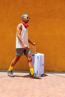 LGBTQIA+ person with colorful style walks confidently with a suitcase, preparing for a holiday.