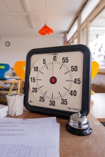 Timer and table bell on a table full of papers in a bright classroom, homework supervision,