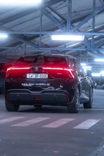 Black car with illuminated tail lights in an illuminated multi-storey car park, e-car sharing, Deer