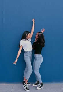 Two young friends share earphones and dance happily against a blue background. They wear casual