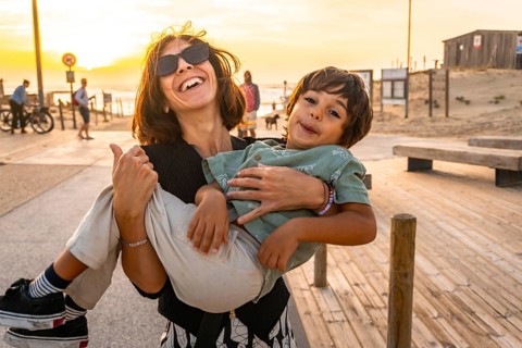 Mother carrying a happy young son, both smiling and making silly faces, enjoying a summer holiday