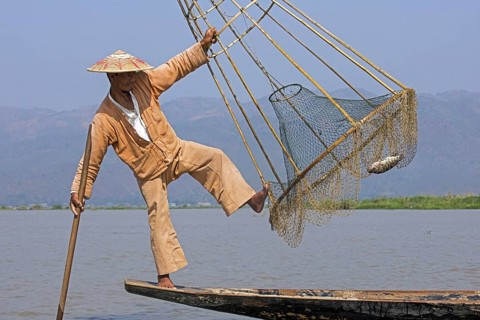 Intha fisherman balancing while holding conical bamboo frame with fishing net, Inle Lake,