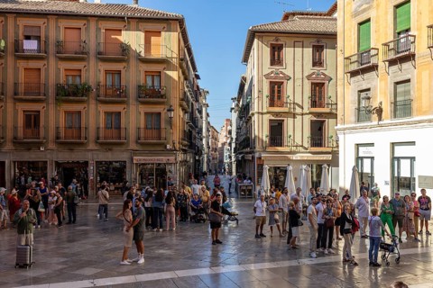 Crowd in a lively, historic town square in sunny weather, Granada