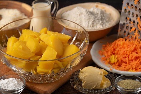 Sliced potatoes and grated carrots next to flour, milk and butter