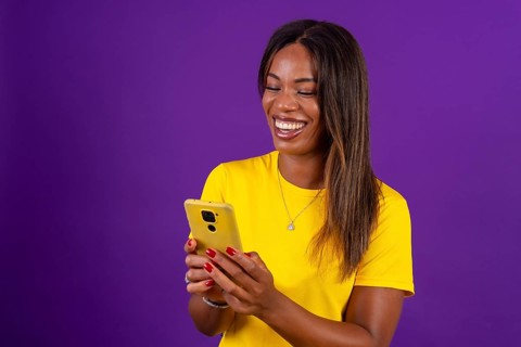 Studio portrait with purple background of a happy african urban woman using mobile phone while
