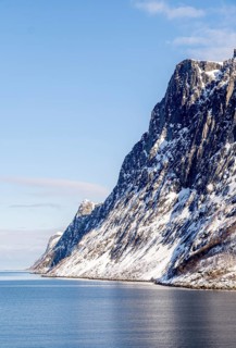 Serene snowy mountains rise dramatically above the tranquil sea in Mefjordbotn, Norway, showcasing
