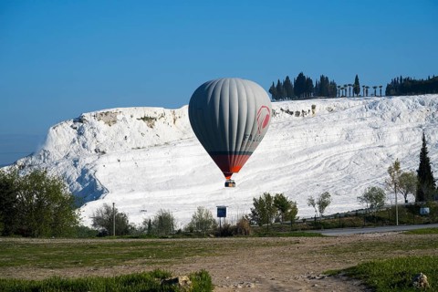A hot air balloon floats in front of white limestone terraces and a blue sky, sinter terraces, lime