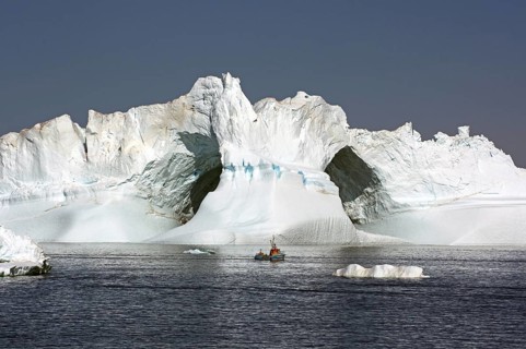 Small fishing boat in front of iceberg with large ice cave, Ilulissat, Disko Bay, Denmark,