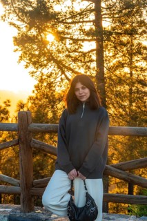 Young woman posing in front of a wooden fence with pine trees and golden sunset light in the forest