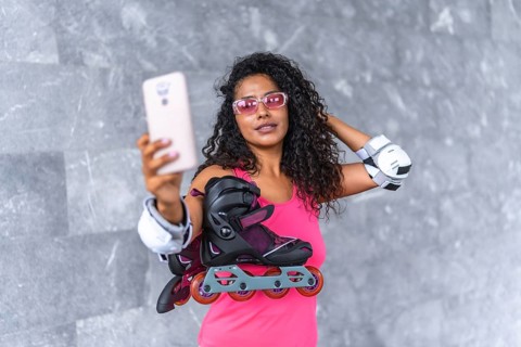 Confident latin woman taking selfie holding inline skates outdoors standing on a urban space