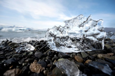 Ice, piece of ice with hole on black gravel beach, glacier lagoon Jökulsárlón, glacial lake,