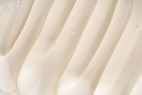Close-up of a creamy cosmetic gel texture featuring smooth, flowing ridges. The soft beige color
