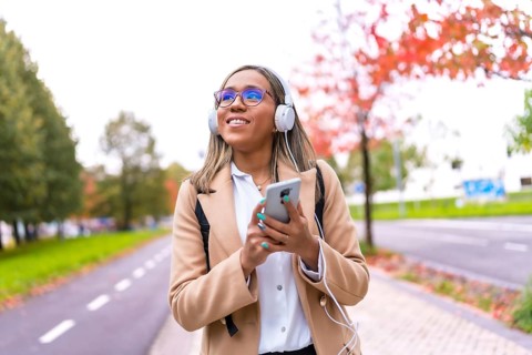 Pretty latin woman using phone and listening to music walking down street