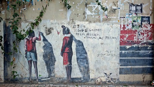 Two people and a dog as silhouettes on a colorful wall full of graffiti, 'pela musica', Ribeira