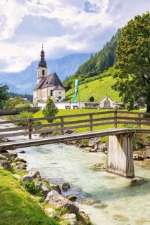 Parish church of St Sebastian by a river in an idyllic Alpine landscape with mountains and forests