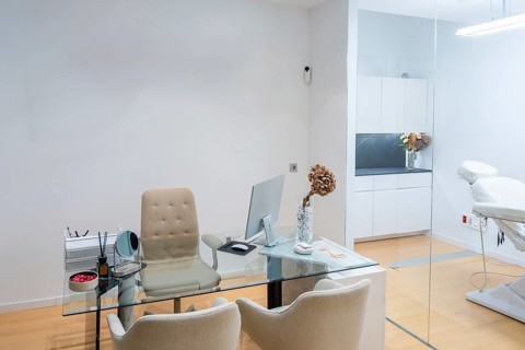 Contemporary aesthetic clinic interior featuring a glass desk workstation with computer and office