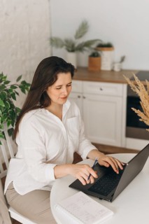 A nutritionist in a bright home office setting, using a laptop. The space is decorated with plants