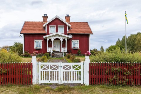 Typical Swedish red house with garden fence and flag pole with Swedish flag, Kalmar län, southern