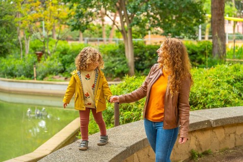 Girl walking on rail holding the hand of her mother along a park next to a pool