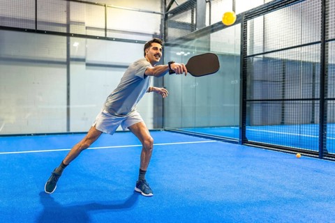 Male athlete with enthusiastic expression hitting a yellow ball with a paddle, actively engaging in