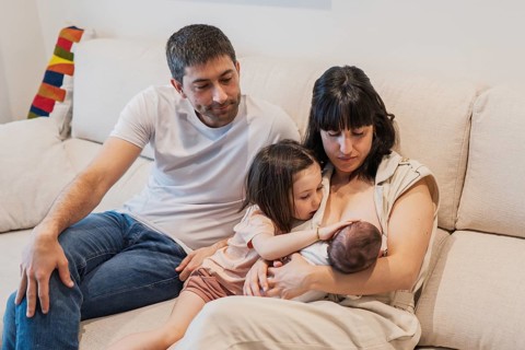 A joyful young family is gathered on a cozy sofa, where a mother holds her newborn baby as the