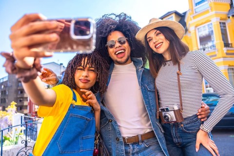 Three joyful tourists capturing a fun selfie with a smartphone in a vibrant city center,