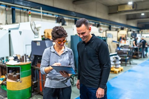 Businesswoman with male caucasian worker talking and inspecting a cnc factory writing notes on
