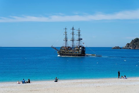 A pirate ship sails off a quiet beach in the blue sea under clear skies, Ölüdeniz, Fethiye, Mugla,