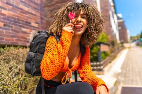 Latin beauty woman playing with lollipop sitting on the street