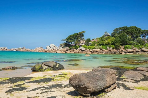 Beach with rocks and sand at the Plage Saint Guirec, with clear blue sky and colors as in the