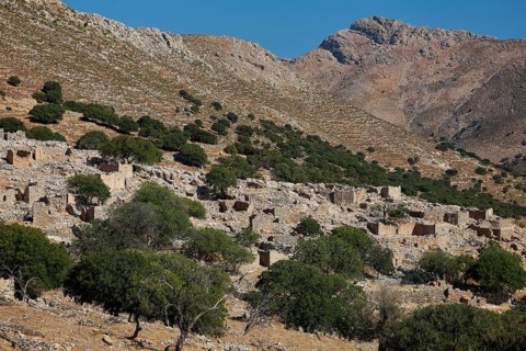 Stone ruins in front of a rocky mountain landscape with scattered trees and blue sky, Lost Place,