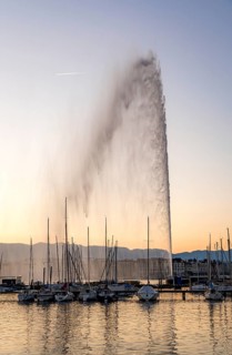 Iconic Jet d'Eau fountain in Geneva shoots water high into the air, backed by a sunset sky and