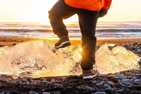 Unrecognizable person at sunrise on Diamond Beach Iceland in winter, resting foot on giant chunk of