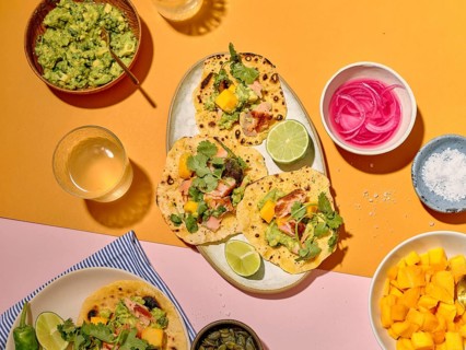 Top view of a taco meal preparation on a vibrant yellow and pink background. The image displays