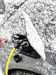 Charging an electric vehicle in winter. A yellow charging cable is connected to the car's charging