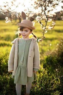 A young girl dressed in a pastel green dress and cozy beige cardigan, wearing a whimsical bunny