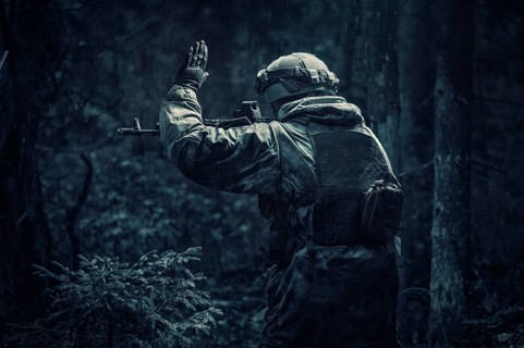 Portrait of a soldier walking through the forest. He raised his hand to warn his partner about the