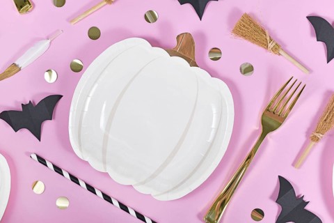 Halloween party flat lay with pumpkin shaped paper plates, bats, golden confetti, forks and spoons