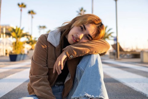 A casually dressed Mixed-race woman sits on a pedestrian crossing on a boardwalk, surrounded by