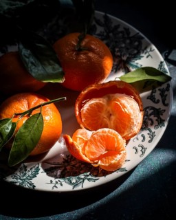 A group of ripe tangerines with vibrant green leaves sits elegantly on a decorative plate. One